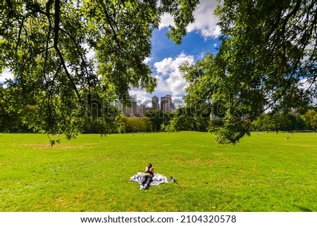 Central Park from Manhattan. Daily life scene and a beautiful day to walk in the biggest park in New York. Great view to the landmarks of this city in America. Woman standing and reading a book.