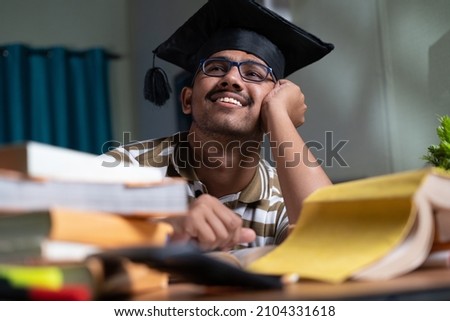 young student dreaming about graduation while studing book or preparing for examination at home - concept of daydreaming and future career goal and education. Royalty-Free Stock Photo #2104331618