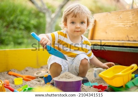 A little boy playing in the sandbox at the playground outdoors. Toddler playing with sand molds and making mudpies. Outdoor creative activities for kids. Royalty-Free Stock Photo #2104341515