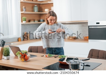 Taking pictures. Woman preparing food at home on the modern kitchen.