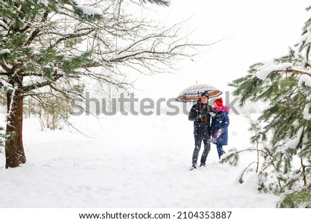 Defocus man in warm hat and child girl on rural winter snowy background holding umbrella. Happy family, cold weather. Time together. Vacations. Snowy winter, lost in forest. Outside. Out of focus.
