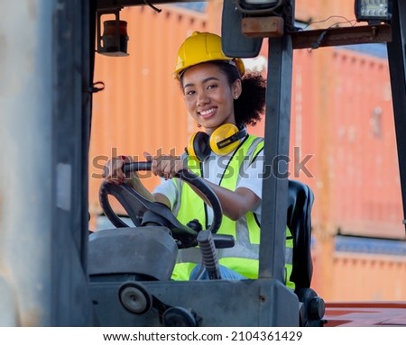 Female foreman wears hard hat driving forklift at shipping container yard, portrait. Smiling mixed race industrial engineer woman in safety vest drives reach stacker to lift cargo box at logistic dock Royalty-Free Stock Photo #2104361429