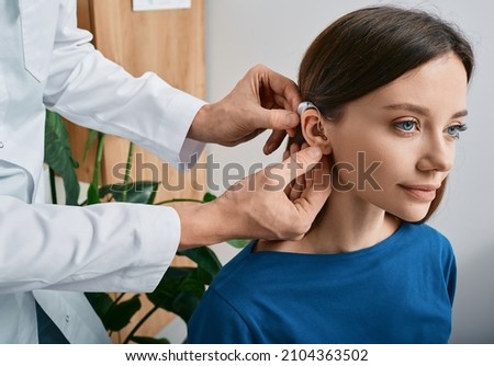 Installation hearing aid on woman's ear at hearing clinic, close-up, side view. Deafness treatment, hearing solutions Royalty-Free Stock Photo #2104363502