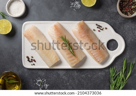 Fresh raw cod fish with lime, spices, herbs, salt and olive oil on a dark background. Healthy food and diet concept. flat lay