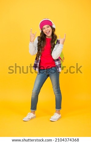Happy girl show rock horn signs listening to music in modern headphones in casual fashion style yellow background, cool