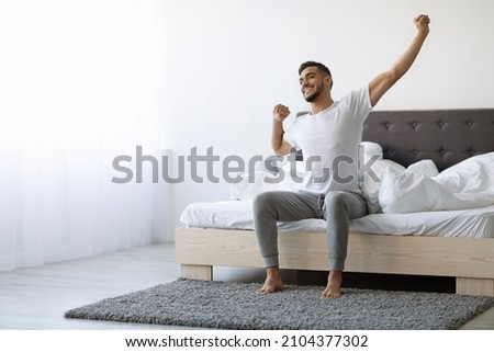 Good Morning. Happy Millennial Arab Guy Sitting On Bed And Stretching After Good Sleep, Handsome Smiling Young Middle Eastern Man Relaxing In Cozy Bedroom, Enjoying Home Comfort, Copy Space Royalty-Free Stock Photo #2104377302