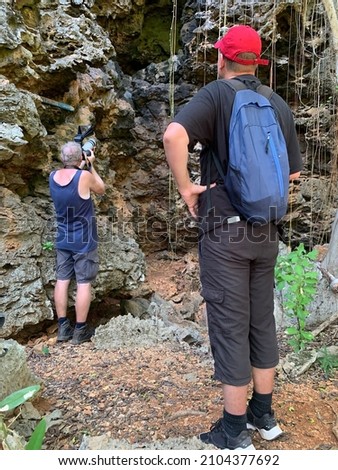 men climbing towards a long narrow cave with bats flying around in an old coral reef hilly range and making pictures of the bat cave