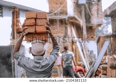 Indian Labour carries pile of bricks on his head  Royalty-Free Stock Photo #2104381133