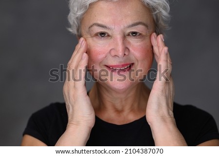 Portrait of Beautiful Senior Woman gently Applying Under Eye Face Cream. Elderly Lady Makes Her Skin Soft, Wrinkle Free with Natural anti-aging Cosmetics