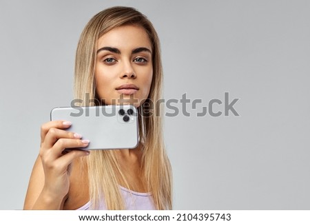 Young beautiful woman using camera in mobile phone isolated on gray background