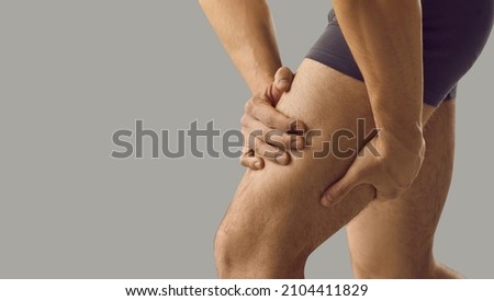 Man feeling pain or having thigh cramp. Sportsman who's suffering from hamstring muscles pain after running, jogging or gym fitness training standing on grey copy space background and touching his leg Royalty-Free Stock Photo #2104411829
