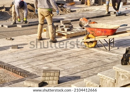 Landscaping company contractors working on interlock driveway project construction site and paving stone bricks. Men working as team to design and construct large home landscape business project. Royalty-Free Stock Photo #2104412666