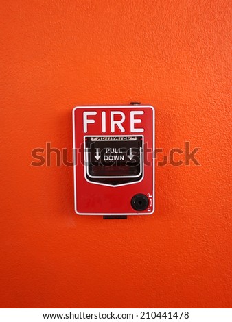 Fire alarm switch on orange wall background.
