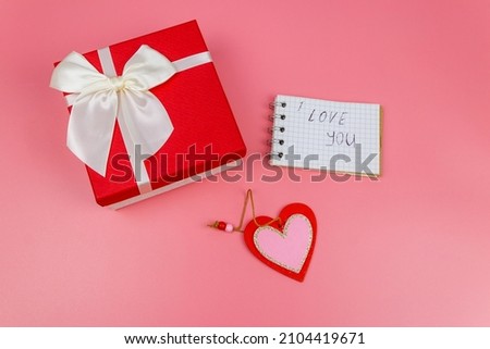Red gift box, Valentine heart and notepad with handwritten text " I Love You" on pastel pink background. Top view, flat lay. Valentine Day concept