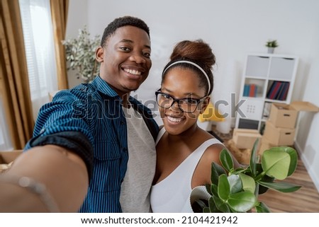 A couple in love moves into their first apartment, they take a picture together with phone on social media after moving in, smiling, happy, bragging about new home, boxes in background Royalty-Free Stock Photo #2104421942