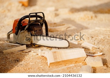 Chainsaw at construction site of wooden houses made of logs lies on background of sawdust.