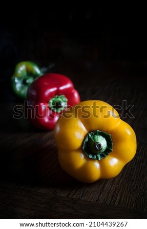 Red bell pepper, green bell pepper and yellow bell pepper on wooden table and dark background