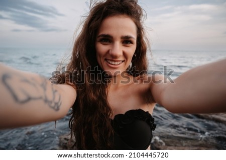 Selfie-portrait of an attractive girl with long hair smiling into the camera close-up, standing against the background of the sea. The concept of tourism, resort, vacation.