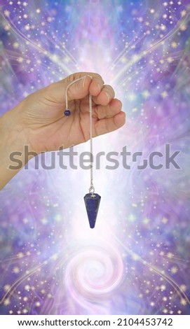 Seven Major Chakras and spiral energy field - female hand holding lapis lazuli dowsing pendant against beautiful sparkling ethereal purple energy background and copy space for messages
