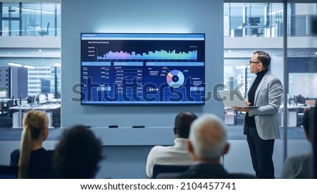Modern Product Presentation Event: On-Stage Successful Caucasian Businessman Speaker Presents e-Commerce Startup Big Data Statistics, Charts, Revenue Growth Infographics. Live Event. Press Conference Royalty-Free Stock Photo #2104457741