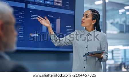 Diverse Modern Office: Successful Black Digital Entrepreneur Uses Tablet Computer and TV Screen with Big Data, Statistics, Talks about Company Growth. Investor, Top Managers, Executives Discuss Graphs
