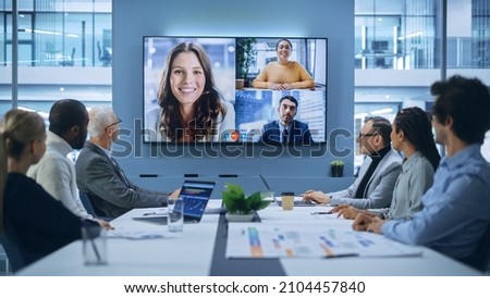 Video Conference Call in Office Boardroom Meeting Room: Executive Directors Talk with Group of Multi-Ethnic Entrepreneurs, Managers, Investors. Businesspeople Discuss e-Commerce Investment Strategy Royalty-Free Stock Photo #2104457840