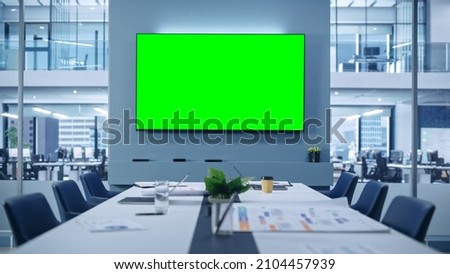 Modern Empty Meeting Room with Big Conference Table with Various Documents and Laptops on it, on the Wall Big TV with Green Chroma Key Screen. Contemporary Minimalistic Designed Workplace. Royalty-Free Stock Photo #2104457939