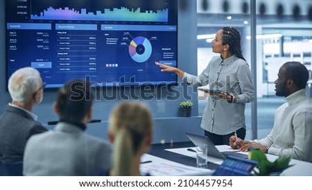 Diverse Modern Office: Successful Black Female Digital Entrepreneur Uses TV Screen with Big Data, Statistics, Talks about Company Growth, Discusses Strategy with Investors, Top Managers, Executives