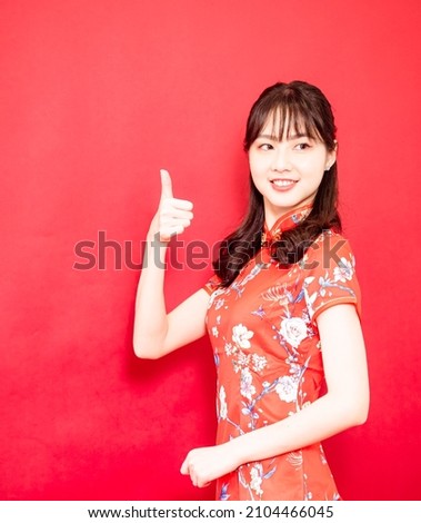 Young asian woman dressing cheongsam with thumbs up gesture, isolated on red background.