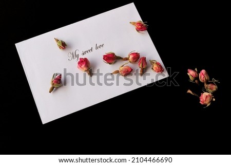white envelope and small red rose buds on black background. Flat lay, top view. Valentine's day concept.