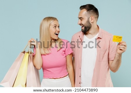 Young happy couple two friends family man woman in casual clothes hold package bags purchases after shopping credit bank card together isolated on pastel plain light blue background studio portrait