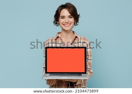 Young smiling happy copywriter woman 20s wearing brown shirt hold use work on laptop pc computer with blank screen workspace area isolated on pastel plain light blue color background studio portrait.
