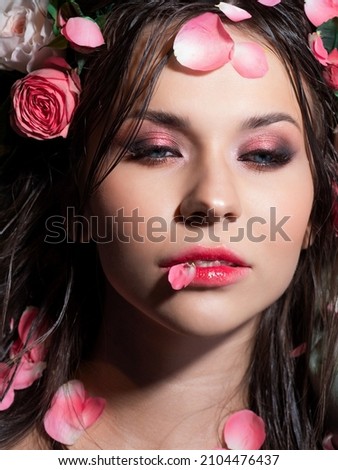 Beautiful blue-eyed brunette with bright pink makeup, lying sprinkled with pink rose petals, close-up, spa and relaxation, concept