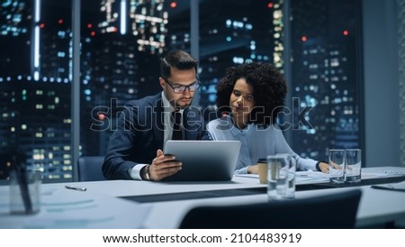 Businesspeople in Modern Office: Business Meeting of Two Managers. Accountant and Operations Director Talk, Discuss, Brainstorm Corporate Strategy, Implementing Budget and Financial Plans. Night. Royalty-Free Stock Photo #2104483919