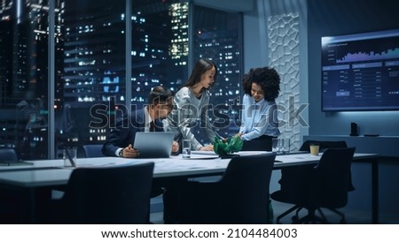 Office Conference Room Meeting: Diverse Team of Top Managers Talk, Brainstorm, Use Laptop Computer. Business Partners Discuss Financial Reports, Plan Operations Based on Line and Pie Graph Reports. Royalty-Free Stock Photo #2104484003
