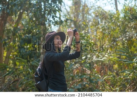 A young woman trekker taking photos of nature with camera in the woods, holidays and traveling concept.