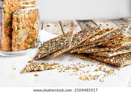 Crunchy crispbread and peanut butter on wooden table. Whole Grain crisp bread with pumpkin, sunflower, chia, linen and sesame seeds. Healthy snack. Bio-organic dieting product. Royalty-Free Stock Photo #2104485917