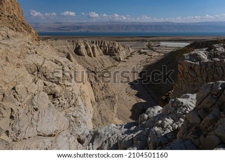 View of Wadi Qumran and the Dead Sea in the background as seen from the trail high above the canyon, located on the northwestern shore of the Dead Sea, Qumran National Park, Israel. Royalty-Free Stock Photo #2104501160