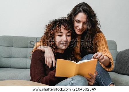 LGBT hispanic lesbian couple reading a book indoor at home - Gay love relationships concept - Focus on girls faces Royalty-Free Stock Photo #2104502549