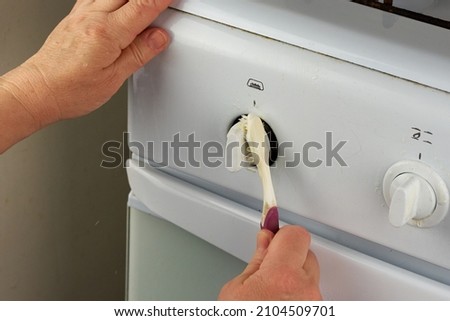 Female hands wash the taps of the white gas stove with a toothbrush. An unusual way of home cleaning