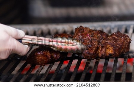 The hand of the cook holds the meat on the coals with a clip.