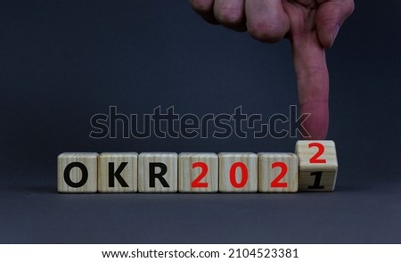 OKR, objectives and key results symbol. Businessman turns a cube with words OKR 2021 and OKR 2022 on beautiful grey background. Business, OKR 2022, objectives and key results concept. Copy space. Royalty-Free Stock Photo #2104523381