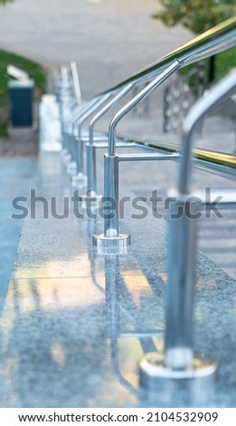 Stainless сhrome steel handrails near the park stairs, close-up. Steps to the city park with railing. Vertical picture.