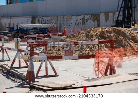 fenced area of the construction site. Red and white safety barriers enclose a pile of soil. There is warning sign on the barrier. Translation: "Danger area! Keep out!"