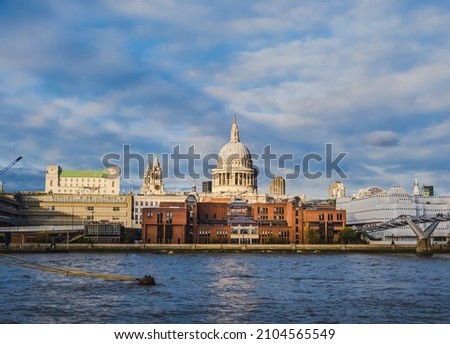 View of St. Paul cathedral in London, England, and buildings around it at sunset from River Thames; blue sky in background