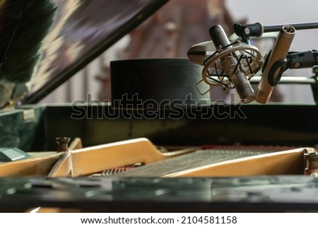 A piano with an open lid. Recording piano playing on a microphone in a recording studio. Large studio microphones.