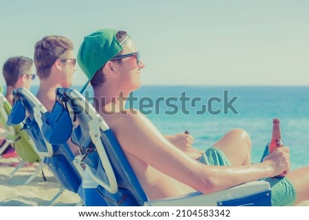 Young men drinking beer in deck chairs on sunny beach
