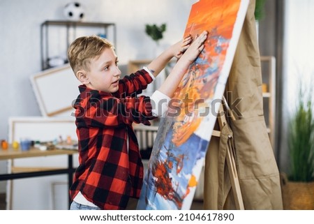Cute caucasian boy dressed in casual clothes drawing abstract pattern on canvas with hands. Little artist is very passionate with creative process at art studio.