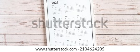 tablet computer with an open app of calendar for 2022 year on a wooden boards background. concept business or to do list goals with technology using. top view, flat lay. banner