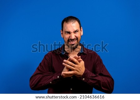 Caucasian man in purple shirt isolated on blue background with covered fingers and looks mysterious to the side has a big evil plan in mind